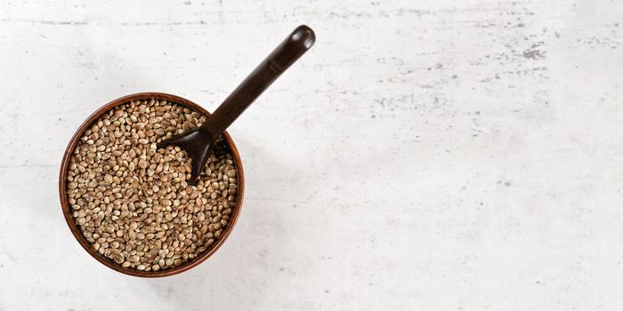 Unpeeled hemp - Cannabis sativa - in small dark wooden cup with spoon view from above, white stone like board space for text under.