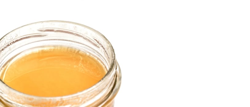 Glass jar with amber colored honey, closeup detail, isolated on white background, space for text right side.