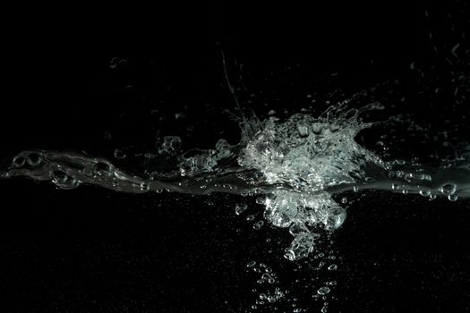 Water splashing as it's poured into aquarium tank, black background.