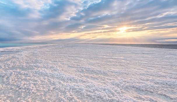 Crystalline white salt beach lit by morning sun, small puddles with seawater at Dead Sea - world most hypersaline lake.