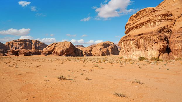 Rocky massifs on red sand desert, bright blue sky in background - typical scenery in Wadi Rum, Jordan.