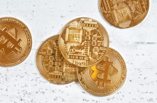 Overhead shot, golden commemorative btc - bitcoin cryptocurrency - coins scattered on white stone board, closeup detail.