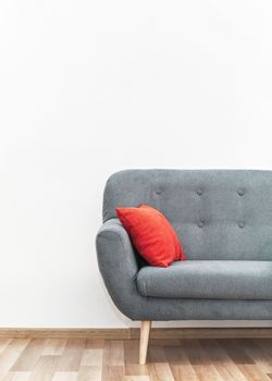 Modern gray couch with red pillows on wooden tiled floor - office furniture, white wall - space for text - above.