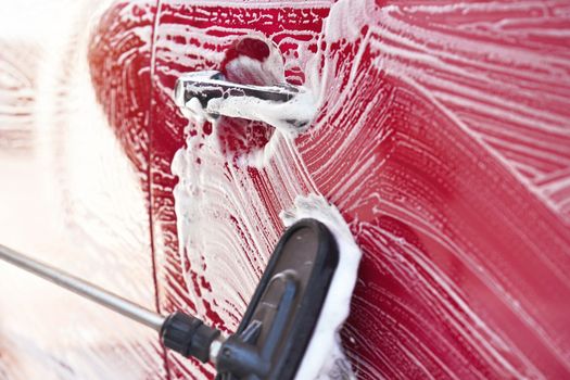 Red car washed in self serve carwash , detail on brush leaving strokes on side door, wide banner with empty space for text left side.