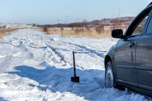 car stuck in snow offroad at daylight with shovel and selective focus.