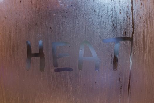 the word heat written on night wet window glass close-up with bokeh background.