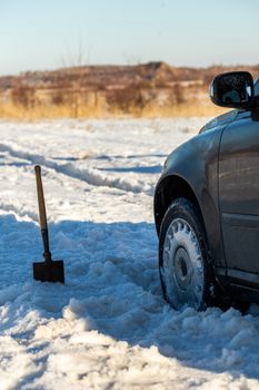 car stuck in snow offroad at daylight with shovel and selective focus.