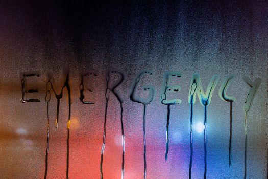 the word emergency written on night wet window glass close-up with blurred background.