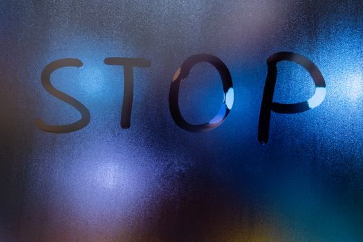 the word stop written on night wet window glass close-up with blurred background.