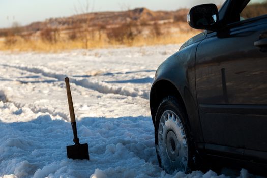 car stuck in snow offroad at daylight with shovel and selective focus.