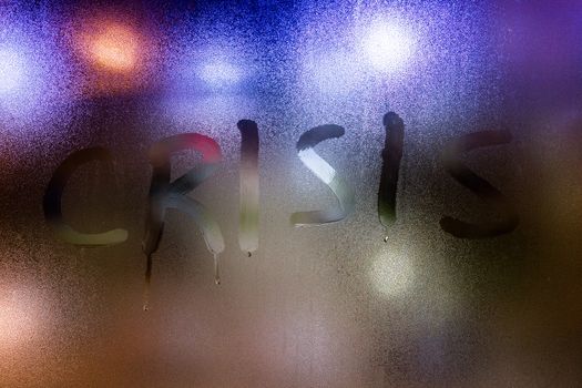 The word crisis written on night wet window glass close-up.