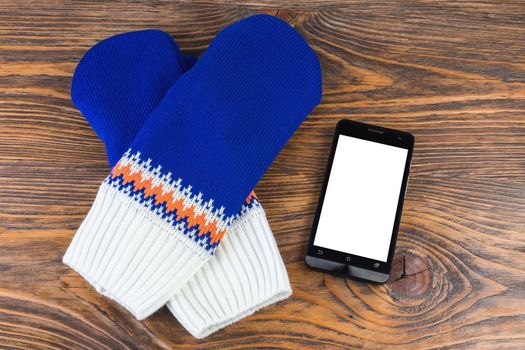 blue and white knited mittens with cellphone on wooden background.