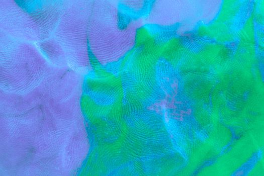 Mixed purple-green-blue flat plastilin texture with distinct finger prints. Small dust particles on bumpy surface.
