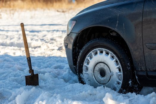 car stuck in snow offroad at daylight with shovel and selective focus.