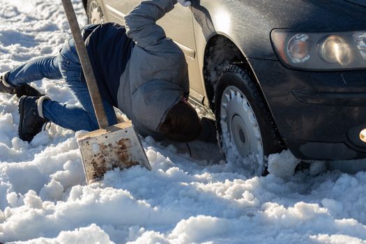 man working at car stuck in snow on knee with shovel at daylight offroad.