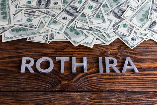 words ROTH IRA laid on wooden surface with metal letters us paper currency