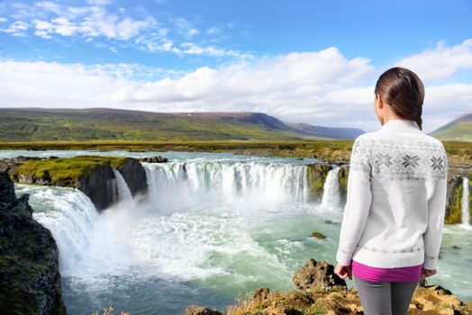 Iceland Travel. Tourist woman by Godafoss waterfall. Happy young woman tourists enjoying icelandic nature landscape visiting famous tourist destination attraction, Iceland.