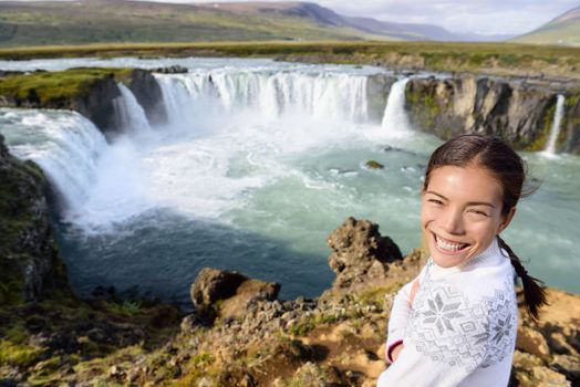 Woman portrait on travel by Godafoss waterfall on Iceland. Happy young woman tourists enjoying icelandic nature landscape visiting famous tourist destination attraction, Iceland.