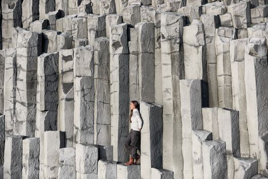 Iceland tourist at beach sitting on basalt columns on Reynisfjara beach, the black sand beach of Vik, South Iceland coast. Happy woman visiting tourist attraction destination.