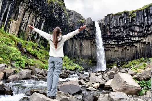 Iceland. Woman enjoying majestic Svartifoss waterfall. Female is visiting famous tourist attraction of Iceland. Spectacular natural landmark on vacation in Skaftafell. Icelandic nature landscape.