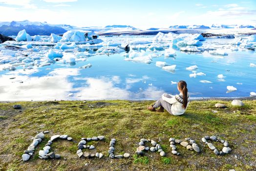 Iceland nature landscape Jokulsarlon glacial lagoon - ICELAND text written with rocks. Woman enjoying view visiting tourist destination landmark attraction glacier lake, Iconic Vatnajokull.