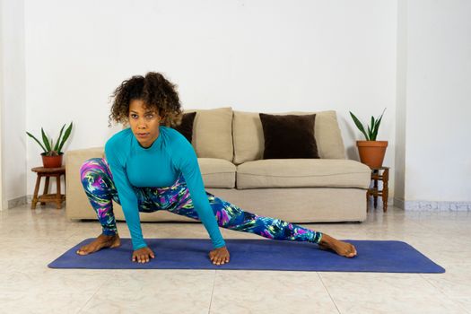 Brazilian black young woman training yoga at home with laptop in living room. Exercising on a mat.