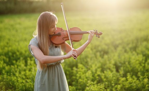 Romantic woman with loose hair playing the violin. Sunset light in nature. Violin training