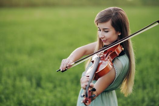 Romantic woman with loose hair playing the violin. Sunset light in nature. Violin training