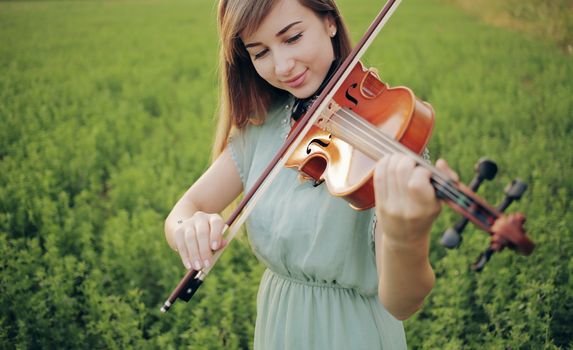 Romantic woman with loose hair playing the violin. Sunset light in nature. Violin training