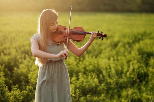 Romantic woman with loose hair playing the violin. Sunset light in nature. Violin training