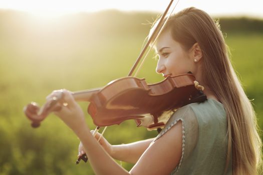 Romantic woman with loose hair playing the violin. Sunset light in nature. Violin training