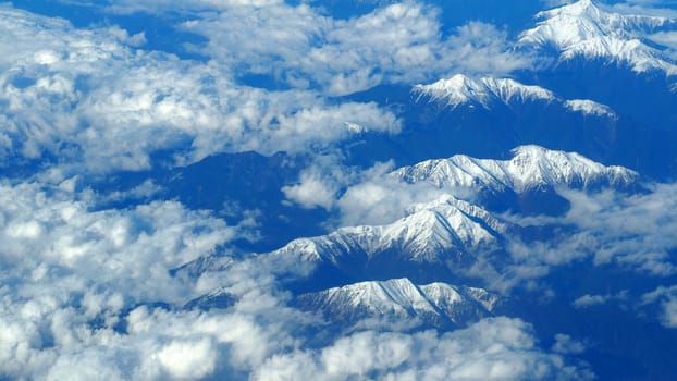 Top view angle images of snow hills around Fuji mountain and white light clouds and blue sky in Tokyo Japan which shoot from airlane.