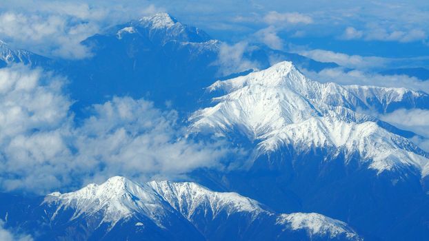 Top view angle images of snow hills around Fuji mountain and white light clouds and blue sky in Tokyo Japan which shoot from airlane.