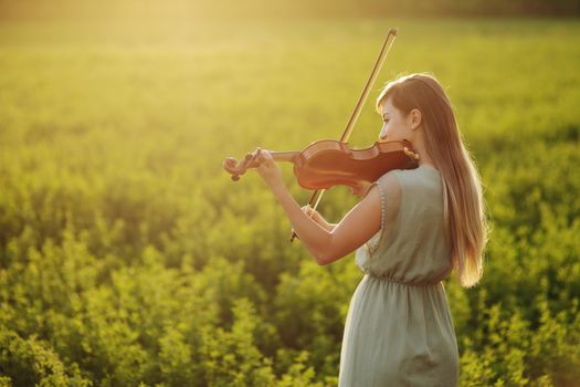 Romantic woman with loose hair playing the violin. Sunset light in nature. Violin training