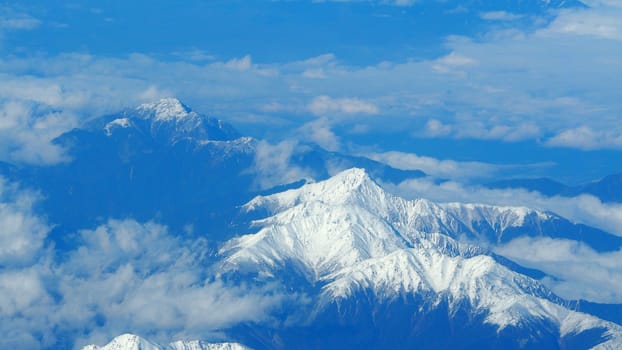 Top view angle images of snow hills around Fuji mountain and white light clouds and blue sky in Tokyo Japan which shoot from airlane.