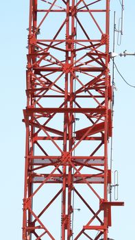 Telecom tower closeup with red color and blue sky.