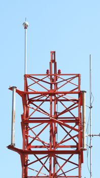 Telecom tower closeup with red color and blue sky.