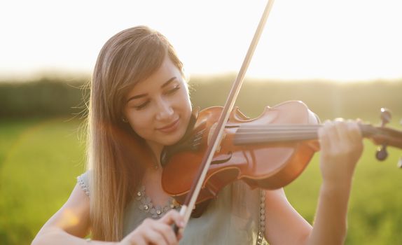 Romantic woman with loose hair playing the violin. Sunset light in nature. Violin training