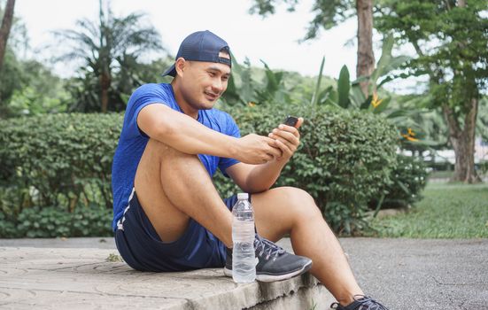 Asian adult men wear sportswear, sit in park after jogging and exercise. Sportsman is using smartphone technology to communicate with many people on Social media. Sports and fitness, healthy concepts