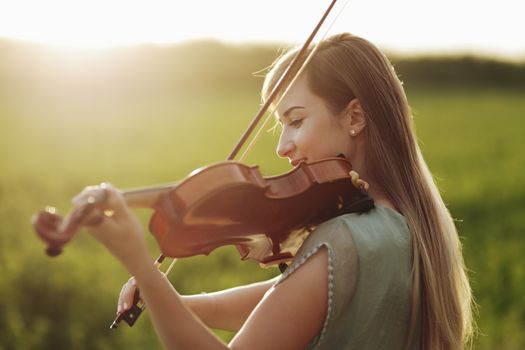 Romantic woman with loose hair playing the violin. Sunset light in nature. Violin training