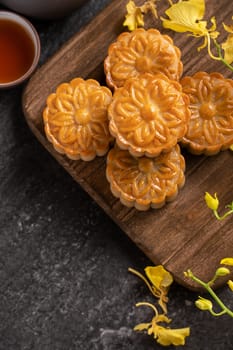 Mooncake, Moon cake for Mid-Autumn Festival, concept of traditional festive food on black slate table with tea and yellow flower, close up, copy space.