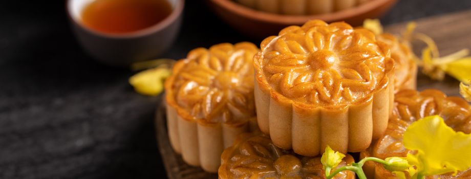 Mooncake, Moon cake for Mid-Autumn Festival, concept of traditional festive food on black slate table with tea and yellow flower, close up, copy space.