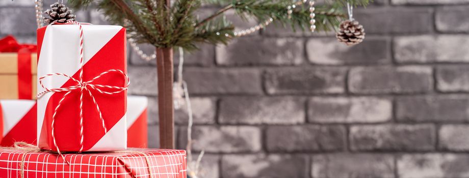 Decorated Christmas tree with wrapped beautiful red and white gifts at home with black brick wall, festive design concept, close up.