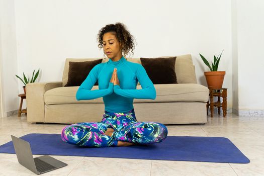 Brazilian black young woman training yoga at home with laptop in living room. Exercising on a mat.