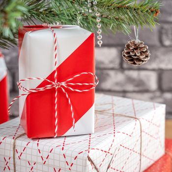 Decorated Christmas tree with wrapped beautiful red and white gifts at home with black brick wall, festive design concept, close up.