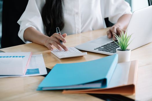 Close up of businesswoman or accountant hand holding pen working on calculator to calculate business data, accountancy document and laptop computer at office, business concept.