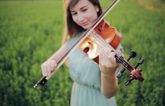 Romantic woman with loose hair playing the violin. Sunset light in nature. Violin training