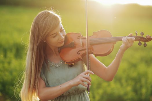 Romantic woman with loose hair playing the violin. Sunset light in nature. Violin training