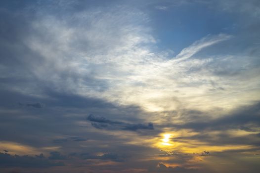 Glowing sun peeking through the clouds at sunset in a twilight blue sky in a nature or weather background with copy space