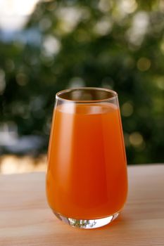 The glass of juice in a garden. The wooden table.